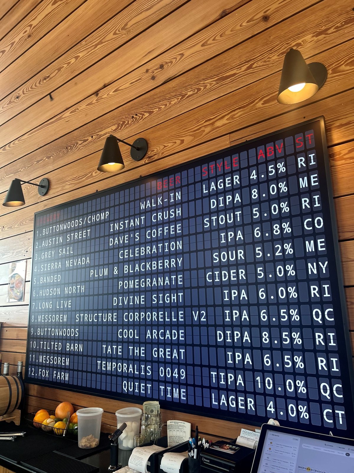 A large split-flap tap list at Chomp in Newport showing twelve beers with brewery, style, ABV and state, on a cedar wall