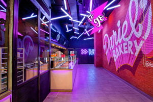 A menuboard and price list on a split flap television at Daniels Bakery