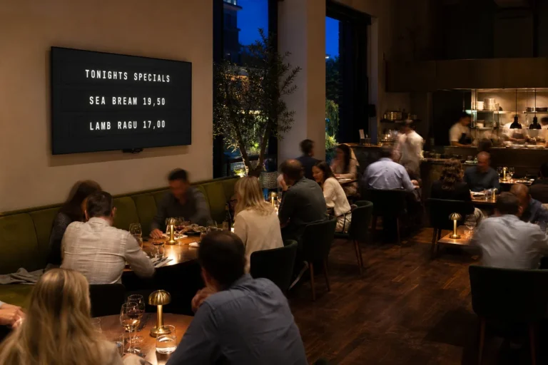 A restaurant dining room with a wall mounted television showing a split-flap style board of tonight's specials.