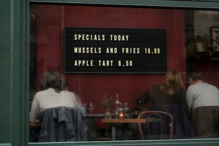 A bistro seen from the street through its window, with a television inside showing a split-flap style specials board.