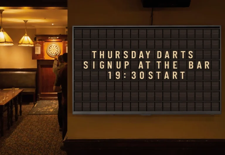 A pub darts room with a television beside the board showing a split-flap style board about the Thursday league.